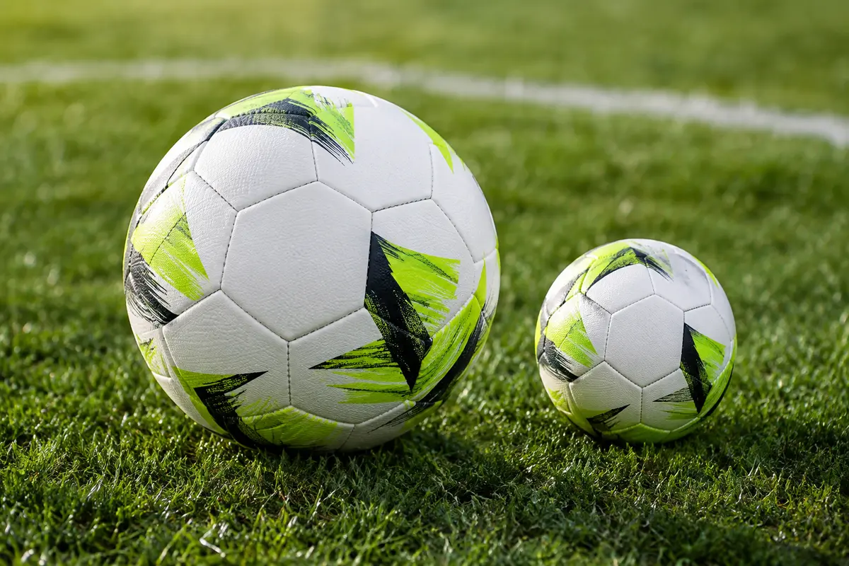 Deux ballons de football de tailles différentes posés sur une pelouse de terrain