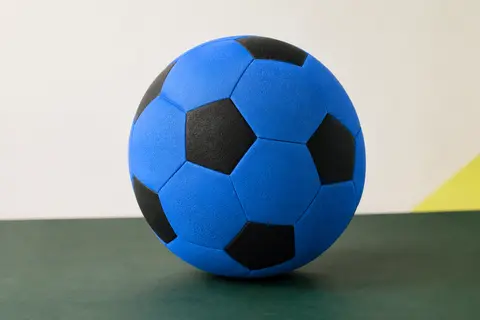 Ballon de football alldoro bleu et noir en mousse, posé sur un fond de studio vert profond