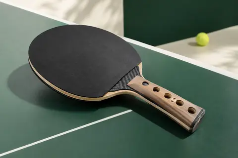 Raquette de tennis de table Cornilleau avec manche perforé et insert carbone, présentée sur une table de jeu