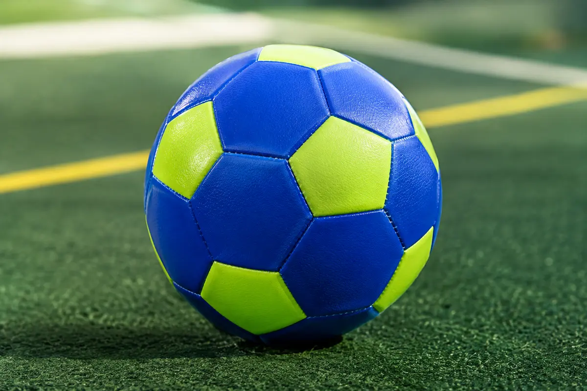 Ballon de football Erima Hybrid Training royal et lime, en polyuréthane texturé, posé sur un fond vert de studio.