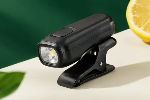 Lampe de course noire à clip en ABS, compacte et rechargeable, présentée sur un fond clair et vert profond.