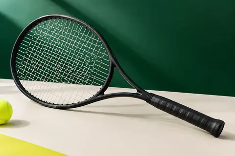 Raquette de tennis adulte noire mate avec tamis cordé et manche souple, présentée sur un fond vert.