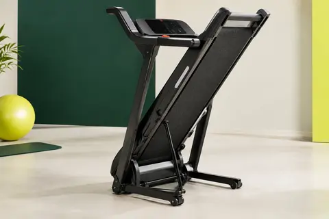 Tapis de course pliable noir avec mains courantes relevées, écran LED et roues, photographié dans un studio clair.
