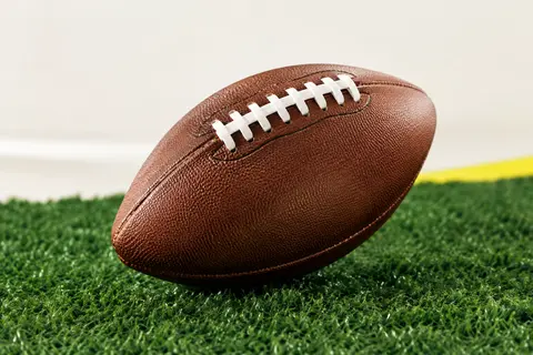 Ballon de football américain marron en composite, avec laçage double, posé sur un fond de gazon vert profond.