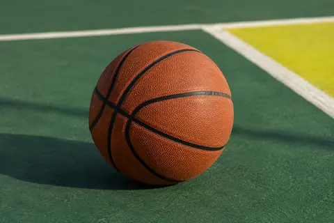 Ballon de basket marron en caoutchouc posé sur un terrain extérieur au décor vert profond