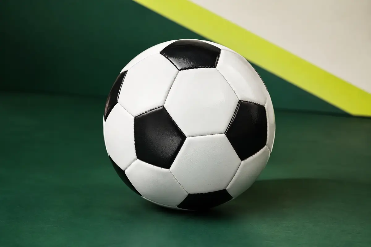 Ballon de football noir et blanc en PVC posé sur un fond vert de studio, avec un panneau vierge.