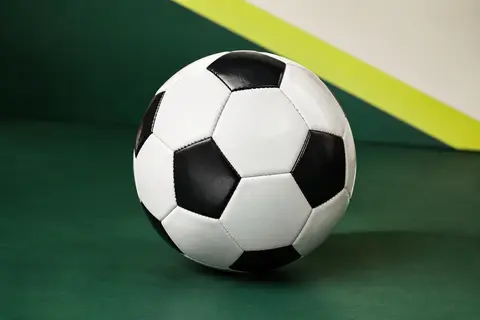 Ballon de football noir et blanc en PVC posé sur un fond vert de studio, avec un panneau vierge.